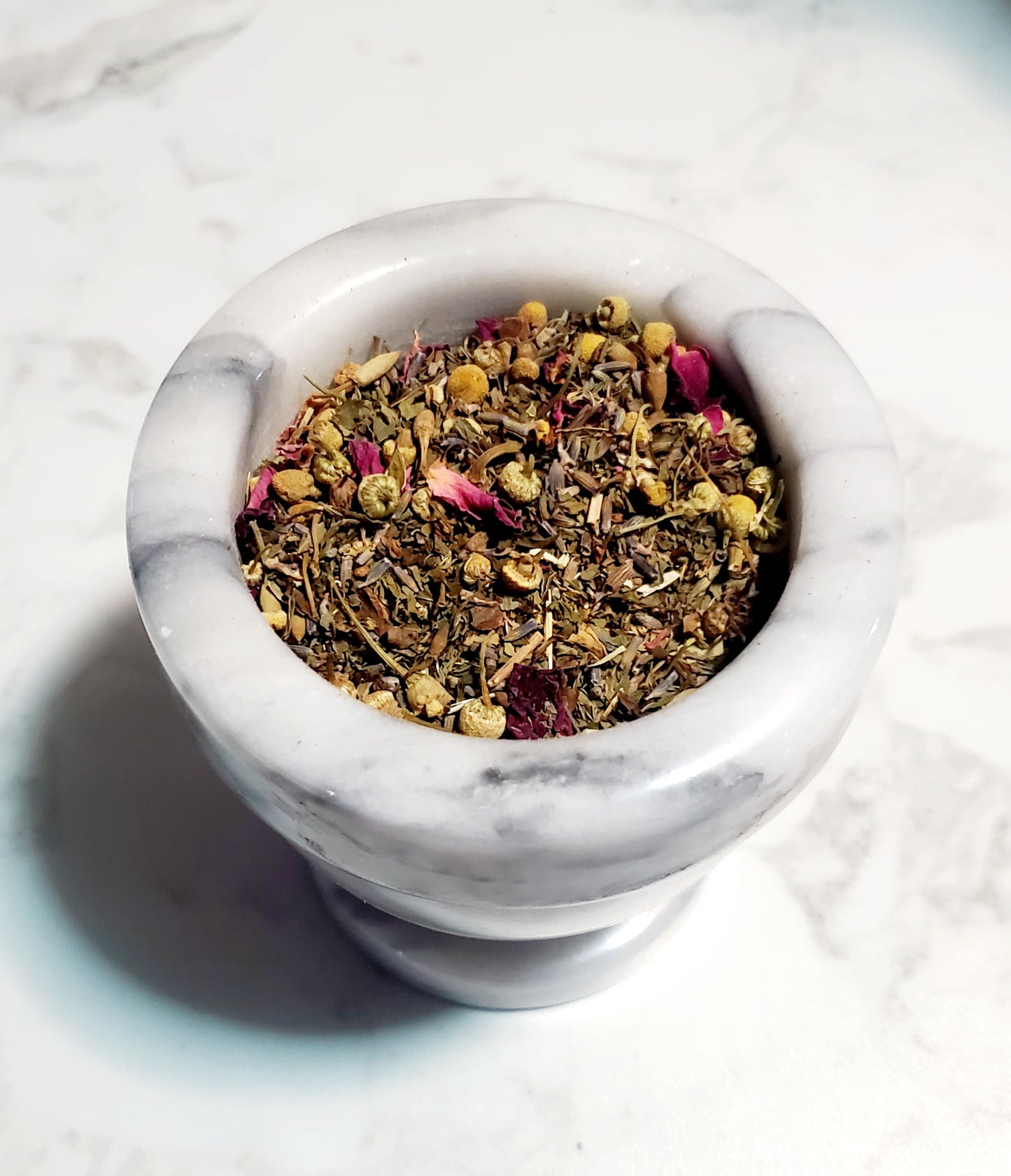 Mortar and pestle with dried herbs on a marble surface.