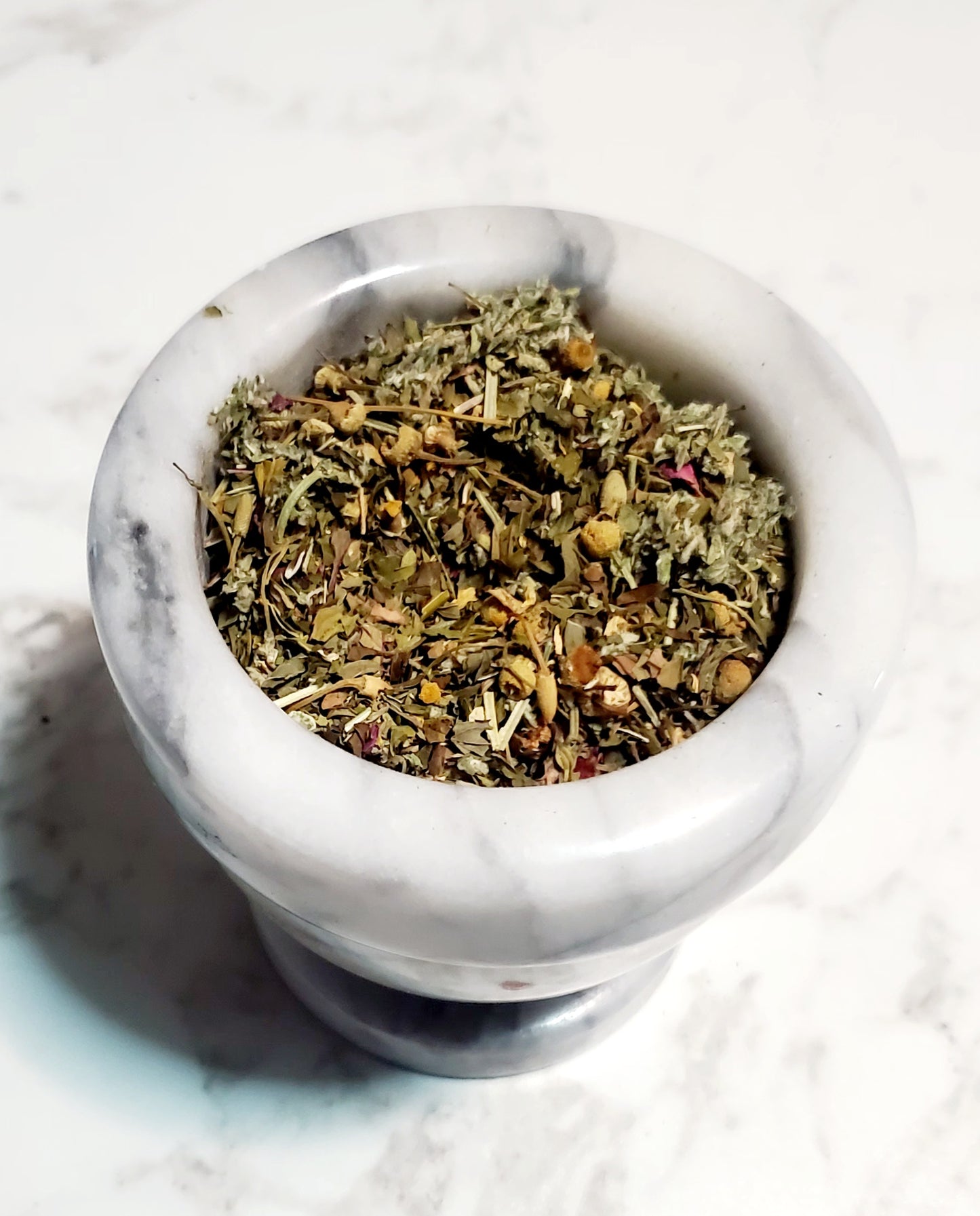 Mortar and pestle with dried herbs on a light background