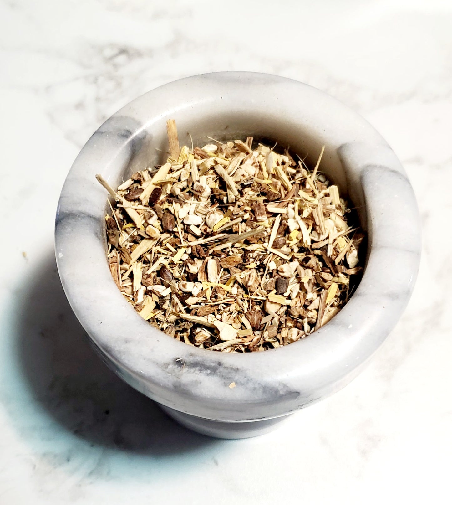 Marble mortar full of dried herbs on a marble background.