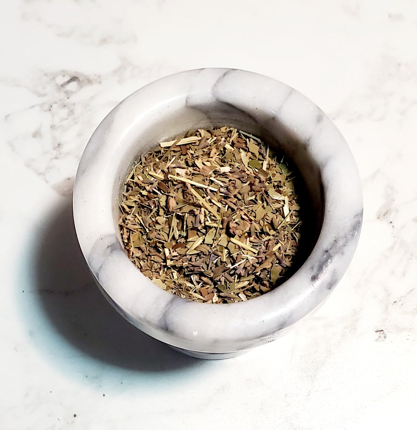 Marble mortar with dried herbs on a marble surface