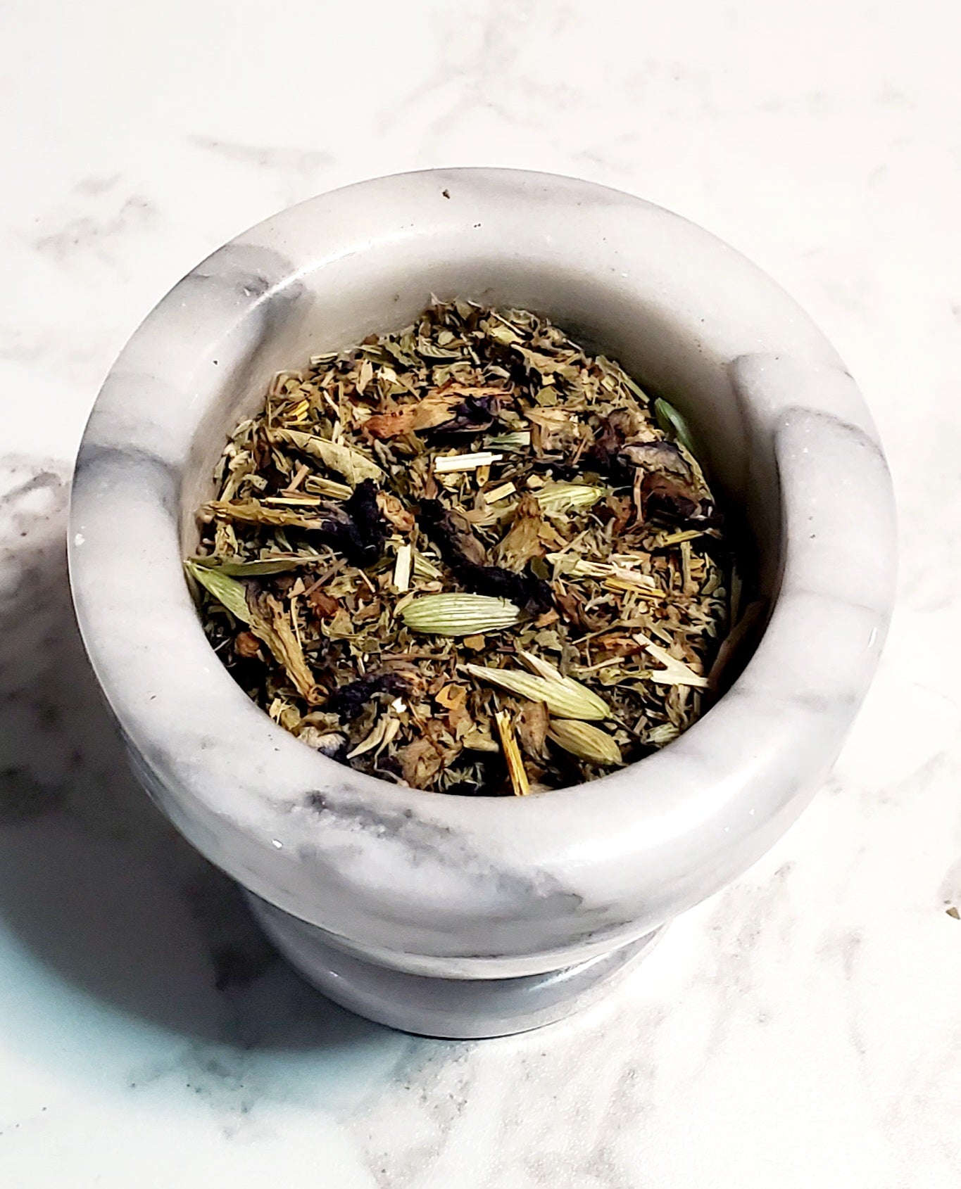 Mortar and pestle with dried herbs on a marble surface