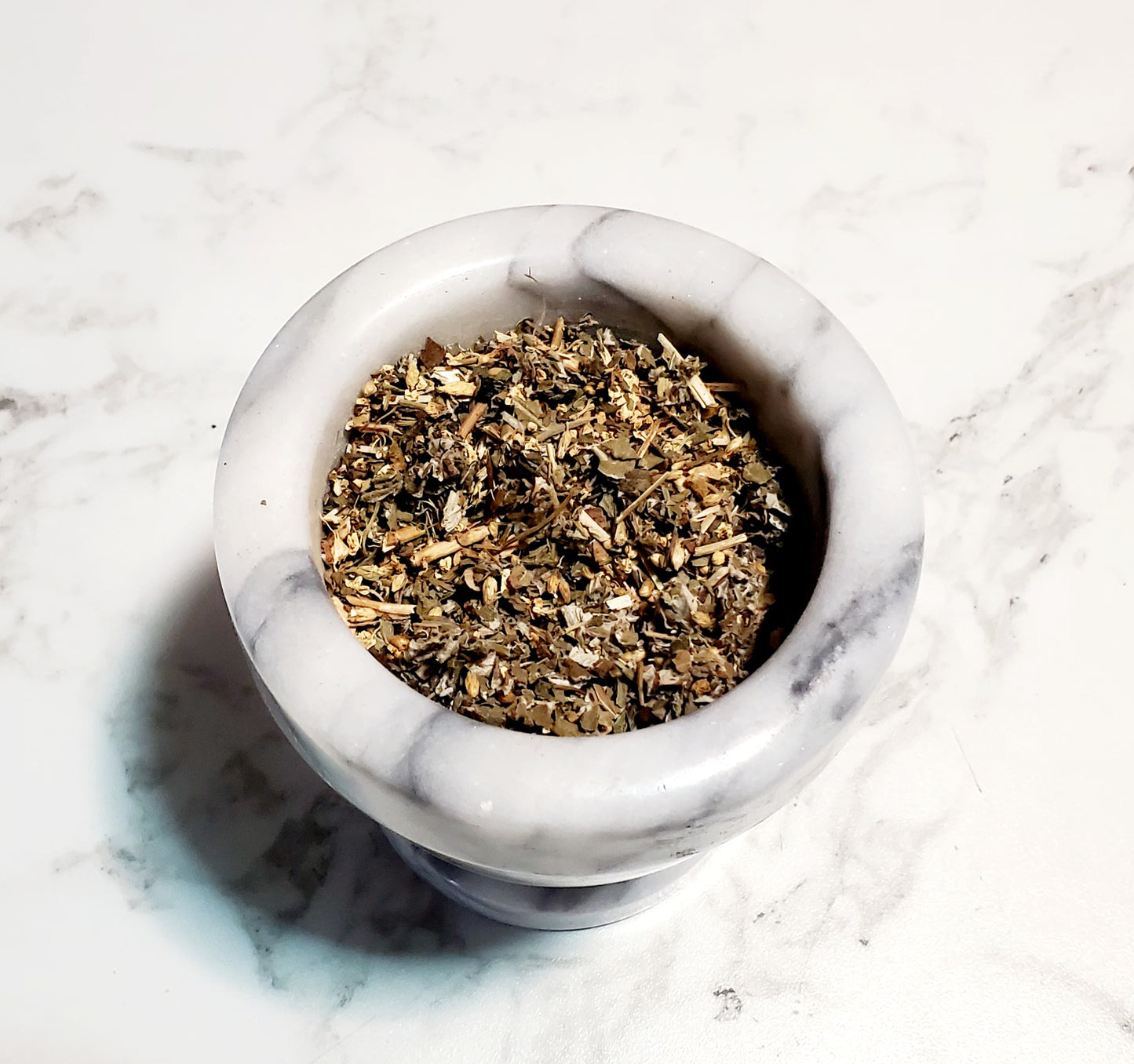 Mortar and pestle with dried herbs on a marble surface