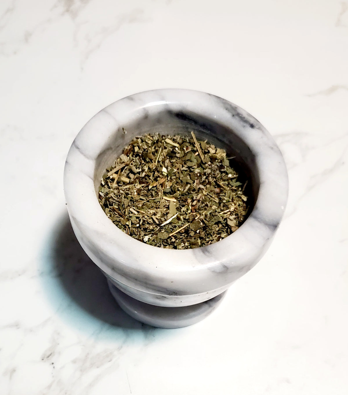 Mortar and pestle with dried herbs on a marble surface