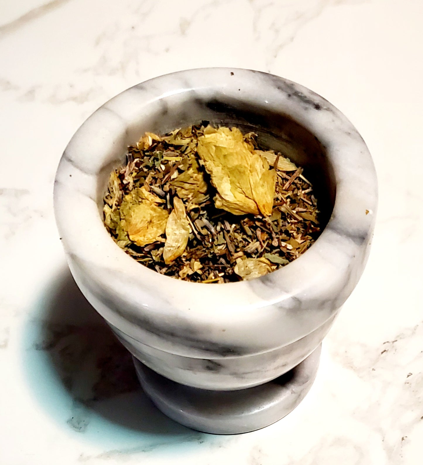 Marble mortar and pestle with dried herbs on a light surface