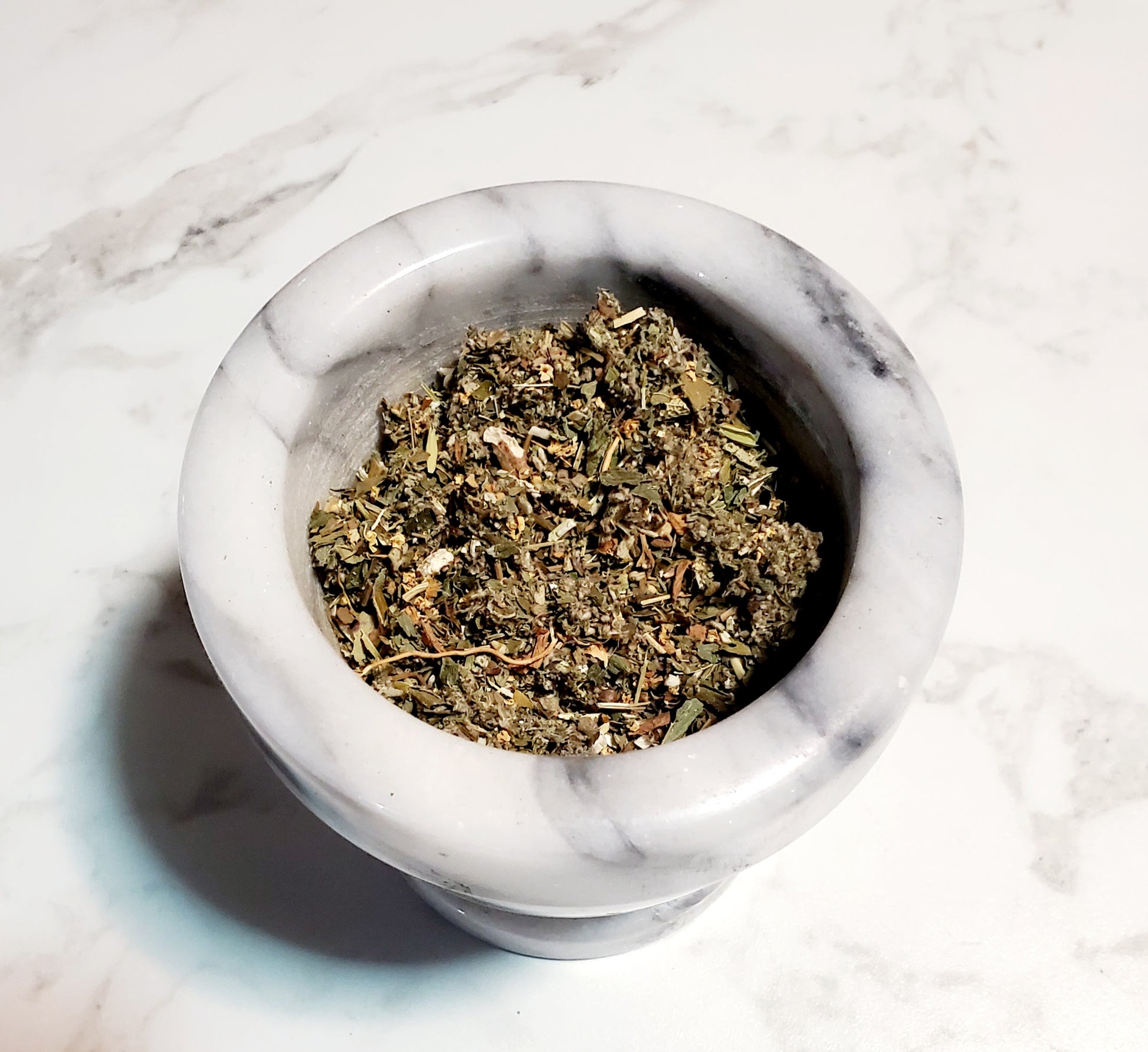 Mortar and pestle with dried herbs on a marble surface