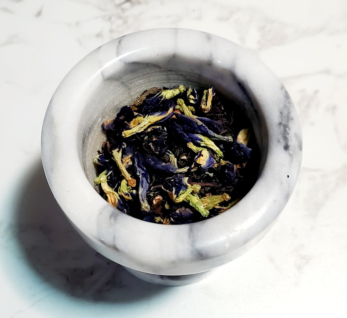 Marble mortar with dried butterfly pea flowers on a marble surface